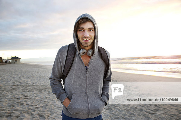 Lächelnder junger Mann am Strand bei Sonnenaufgang