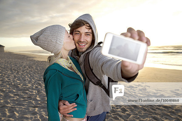 Young couple taking a selfie on beach at sunrise