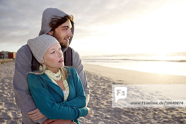 Young couple on beach at sunrise looking on the ocean
