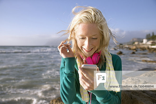 Lächelnde junge Frau mit Handy an der Küste