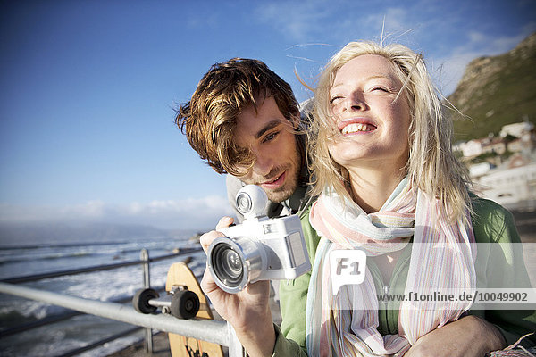 Happy young couple with camera at the coast