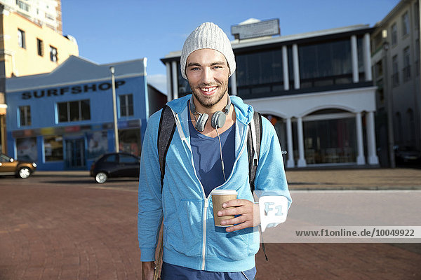 Porträt eines lächelnden jungen Mannes mit Kaffee zum Mitnehmen