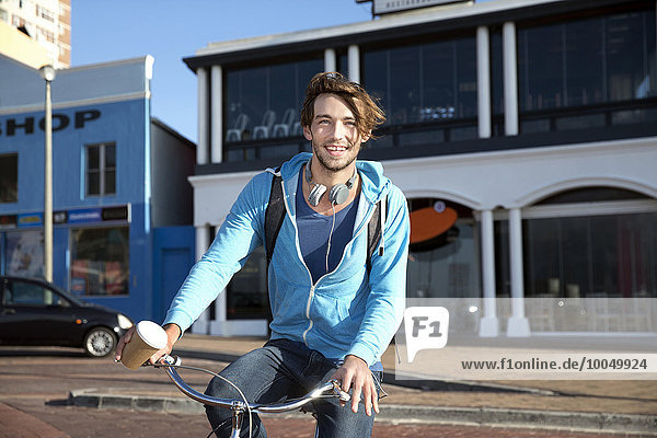Smiling young man holding coffee to go on bicycle