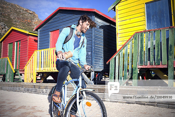 Young man riding bicycle at colorful beach huts