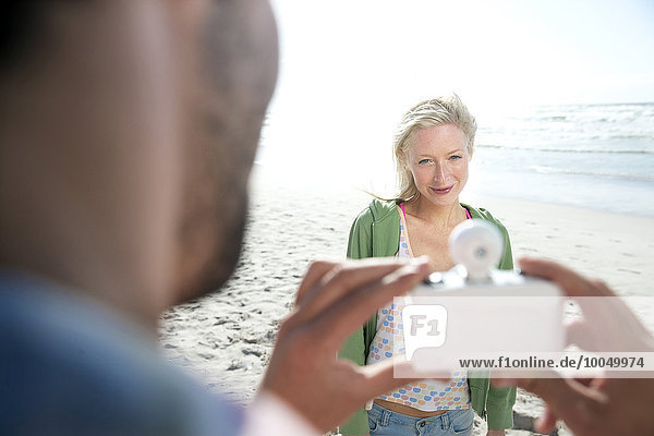 Mann fotografiert lächelnde Frau am Strand