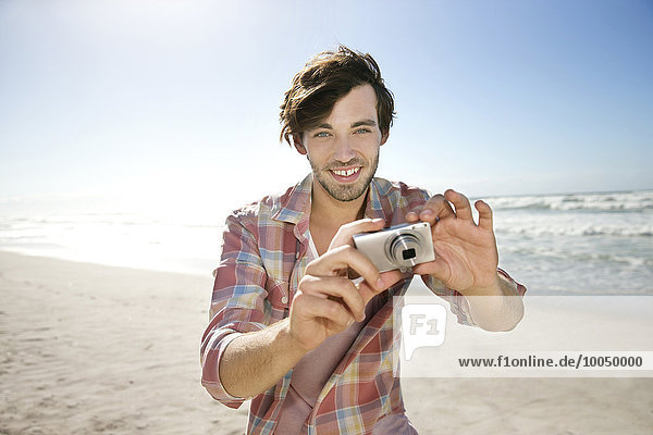 Junger Mann beim Fotografieren am Strand