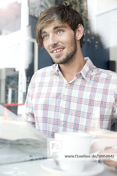 Lächelnder junger Mann in einem Café  der nach oben schaut.