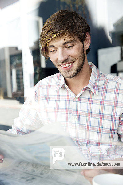 Lächelnder junger Mann in einem Café beim Zeitungslesen