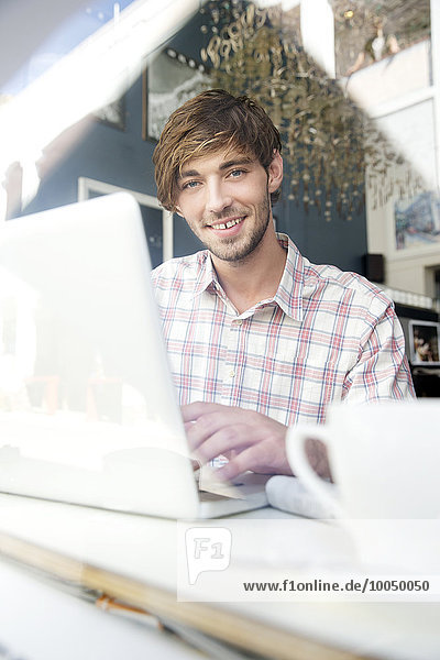 Smiling young man in a cafe using laptop