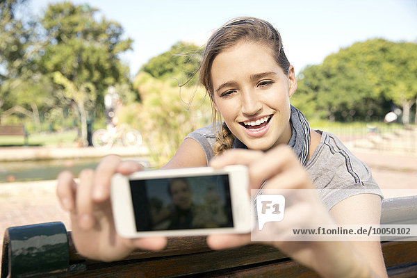 Fröhliche junge Frau auf der Parkbank mit einem Selfie
