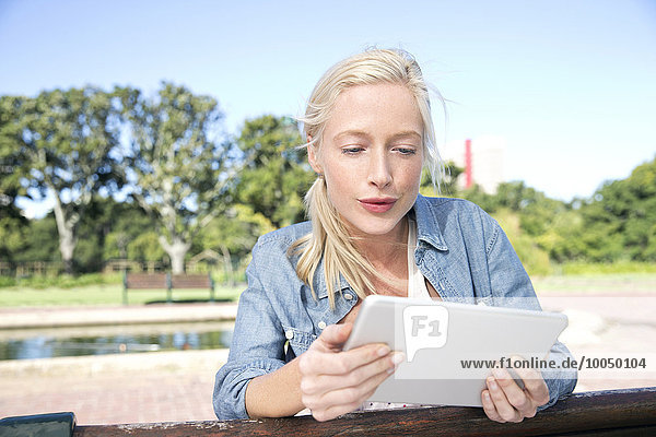 Young woman using digital tablet on park bench