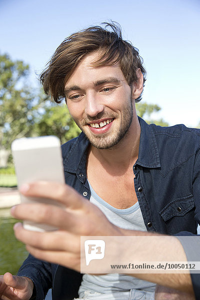 Lächelnder junger Mann im Park mit einem Selfie