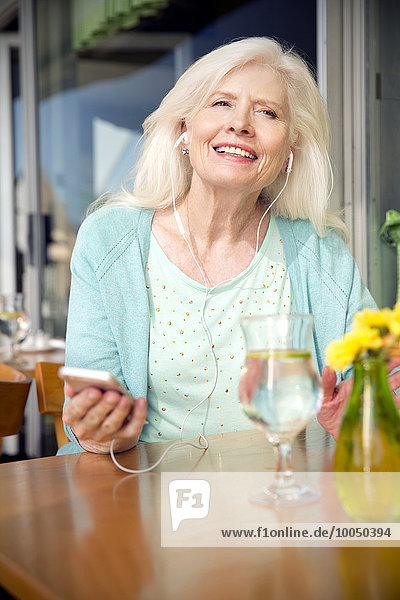 Porträt einer älteren Frau mit Smartphone  die Musik mit Kopfhörern hört.