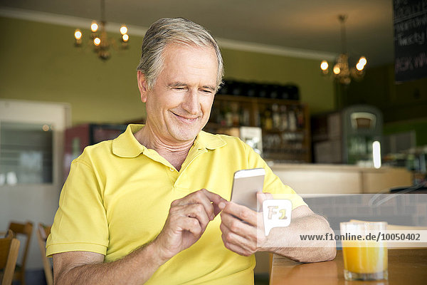 Porträt eines älteren Mannes mit Smartphone in einem Cafe
