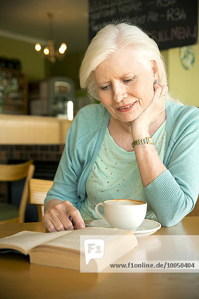 Porträt einer älteren Frau beim Lesen im Café