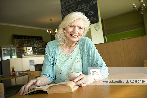 Porträt einer älteren Frau mit Buch im Café