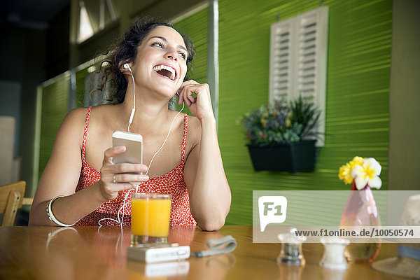 Porträt einer glücklichen Frau  die Musik mit dem Smartphone in einem Café hört.