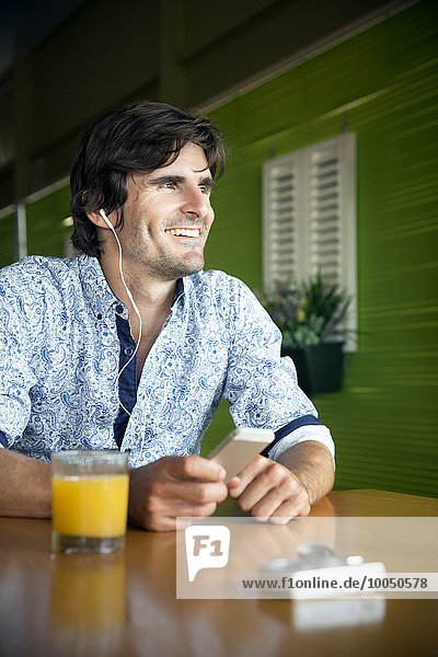 Porträt eines lächelnden Mannes  der Musik mit einem Smartphone in einem Café hört.