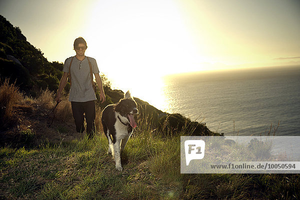 Südafrika  ein Mann  der in der Abenddämmerung mit seinem Hund an der Küste entlang läuft.