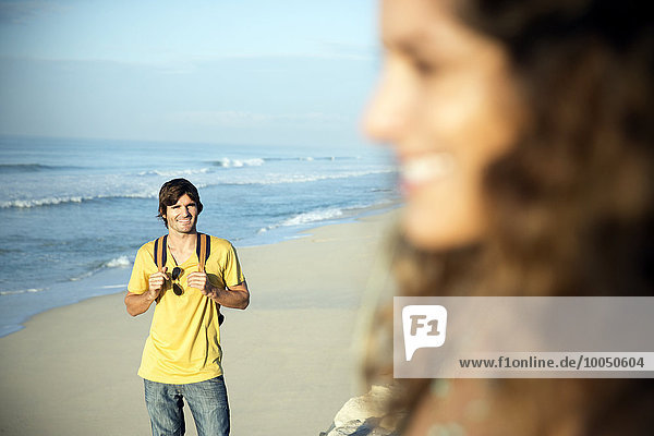 Südafrika  lächelnder Mann  der am Strand steht und seine Freundin beobachtet.