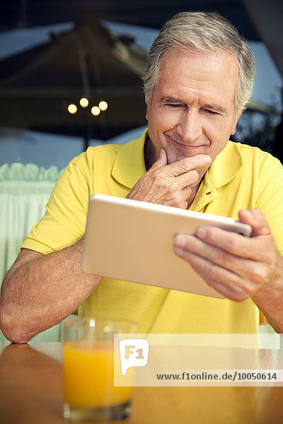 Porträt eines älteren Mannes  der in einem Café sitzt und ein digitales Tablett benutzt.