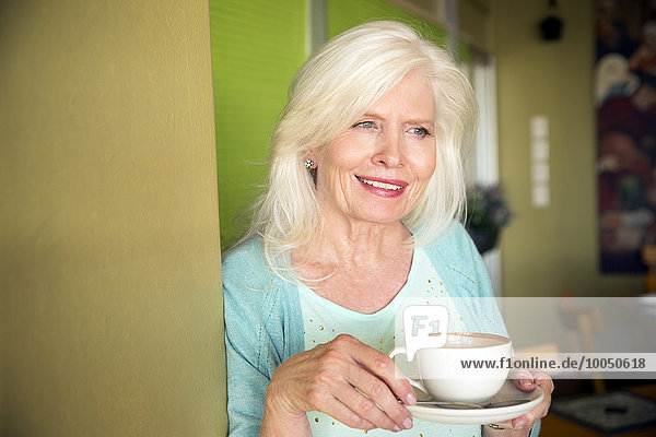 Porträt einer glücklichen Seniorin mit einer Tasse Kaffee im Cafe