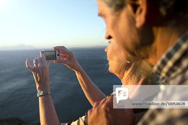 South Africa  senior couple taking a picture of the sea by sunset