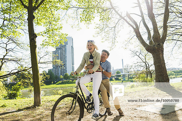 Mature couple riding bike in park  man sitting on rack