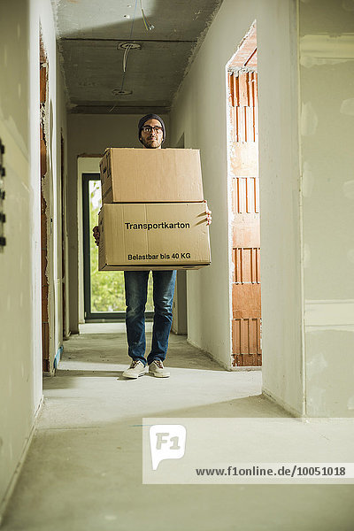 Young man carrying cardboard boxes in hallway
