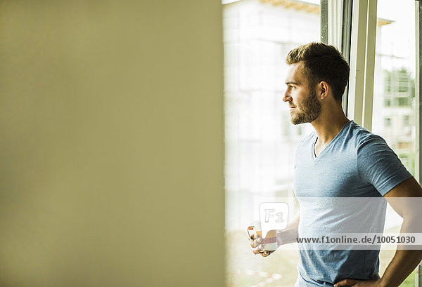 Young man holding coffee cup looking out of window