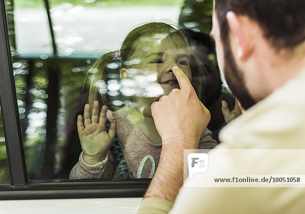 Vater berührt die Nase des Mädchens hinter dem Autofenster