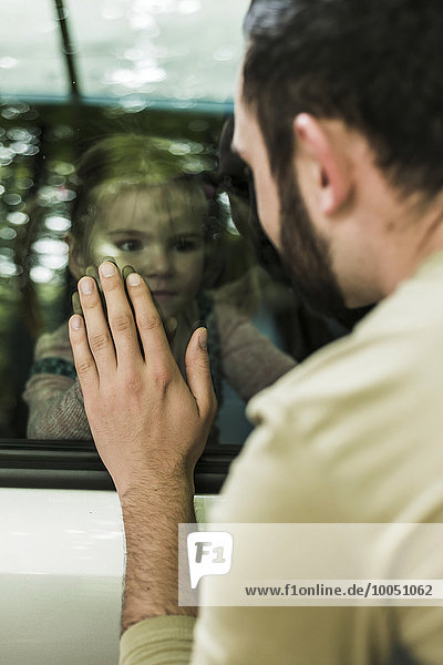 Mädchen im Auto mit Blick auf Vater hinter der Fensterscheibe