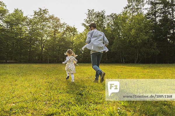 Vater und Tochter laufen mit Papierwindmühle auf der Wiese
