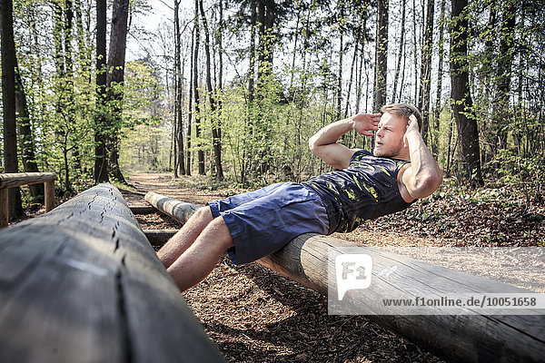 Germany  Coburg  Young man exercising sit ups on a fitness trail in a forest
