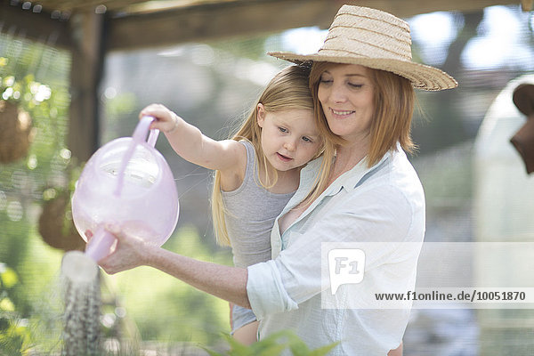 Portrait of woman and little daughter watering plants with watering can