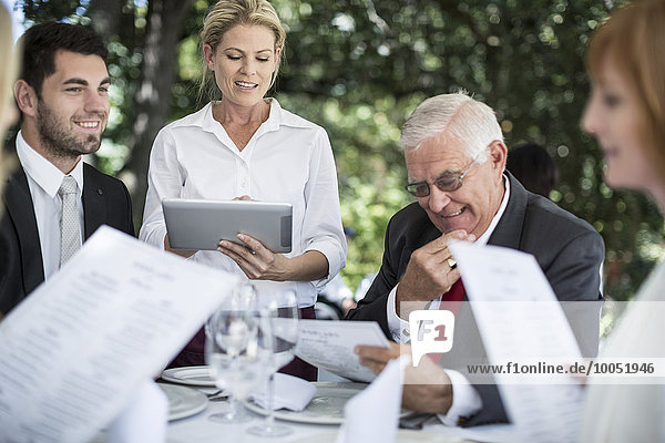 Kellnerin  die ihre Kunden am Tisch mit einem digitalen Tablett zum Mittagessen einlädt.