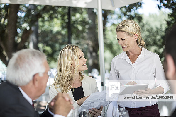 Kellnerin  die ihre Kunden am Tisch mit einem digitalen Tablett zum Mittagessen einlädt.