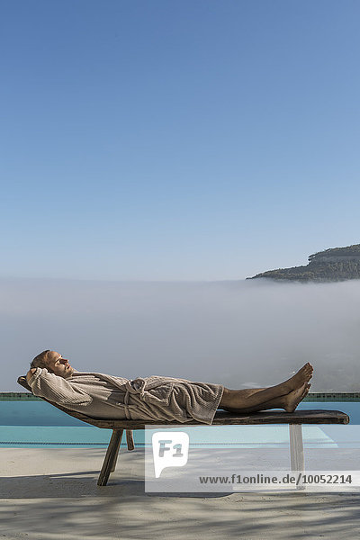 Mann im Bademantel auf einer Lounge neben dem Pool liegend