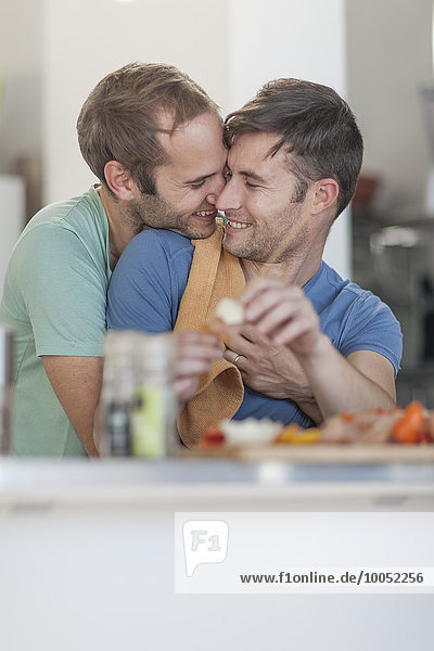 Happy gay couple preparing meat skewers in kitchen