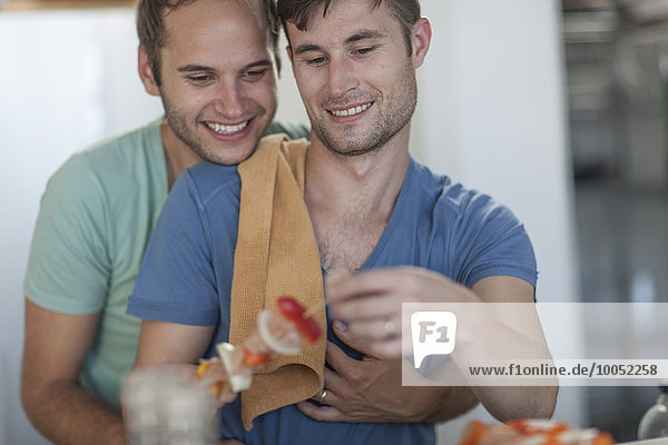 Fröhliches schwules Paar beim Zubereiten von Fleischspieße in der Küche