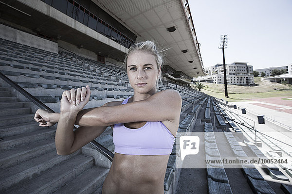 Porträt einer Sportlerin bei Dehnübungen auf der Tribüne eines Stadions
