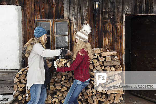Two young female friends stacking logs outside cabin