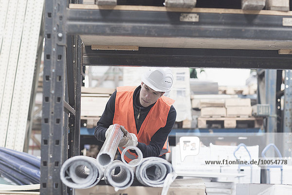 Young male warehouse worker selecting industrial pipe from shelf