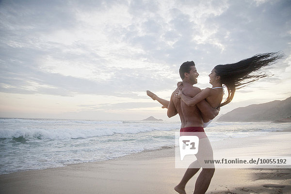 Mid adult couple on beach  man carrying woman in arms  rear view