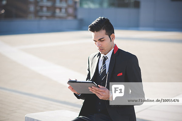 Young businessman using digital tablet on bench