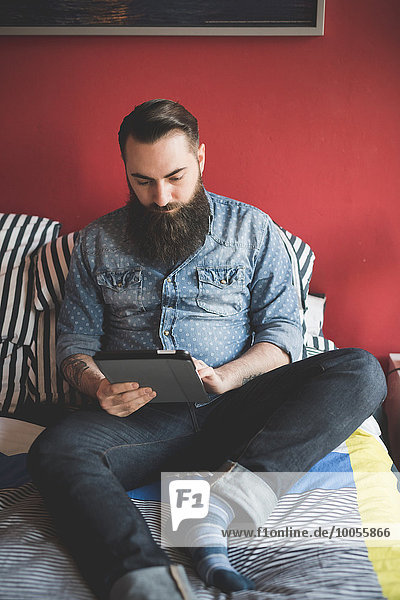 Young bearded man using digital tablet on bed