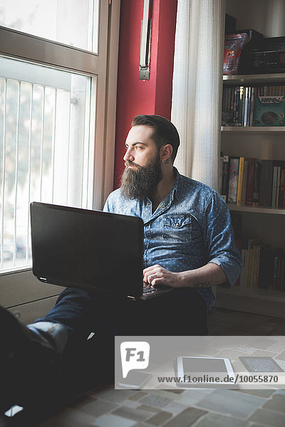 Young bearded man using laptop on floor