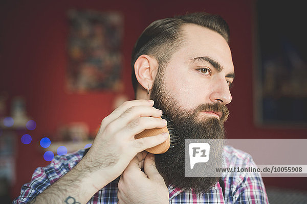 Junger bärtiger Mann beim Bürsten seines Bartes