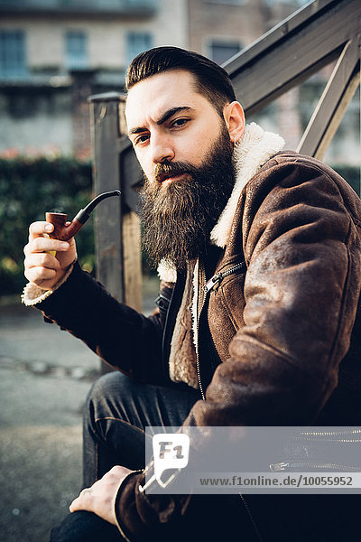 Young bearded man smoking pipe on steps