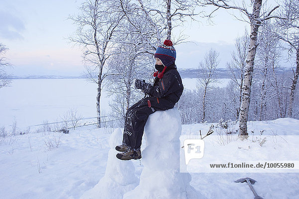 Junge sitzend auf Schneemann  Hemavan  Schweden
